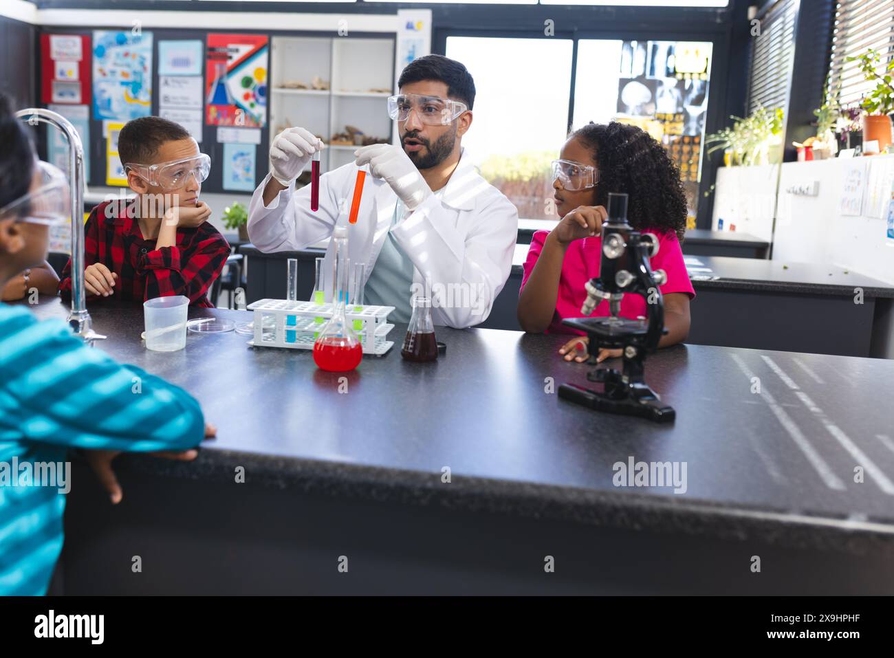 I bambini osservano l'insegnante maschile asiatico che fa test scientifici Foto Stock