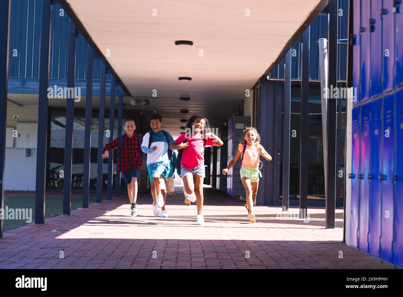 Quattro bambini birazziali corrono gioiosamente attraverso un corridoio scolastico Foto Stock