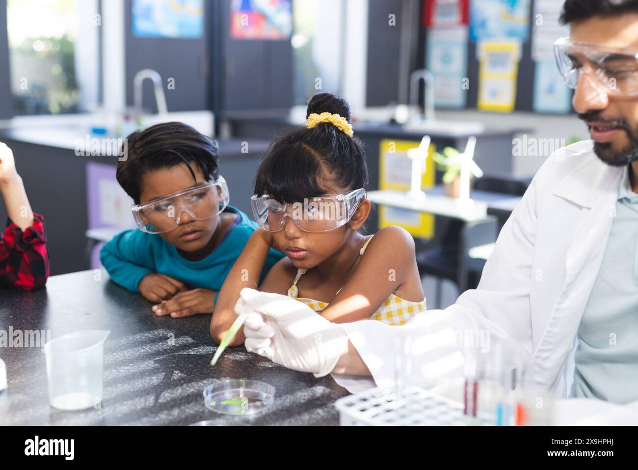 A scuola, insegnante asiatico maschile che mostra due studenti birazziali esperimento scientifico Foto Stock