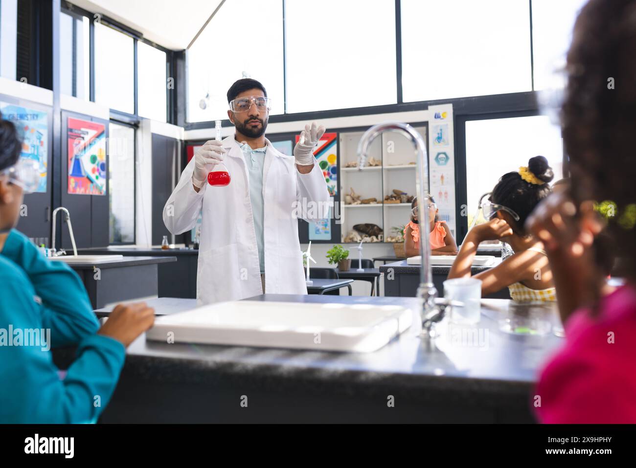 L'insegnante maschile asiatico mostra liquido rosso agli studenti birazziali in un esperimento scientifico Foto Stock