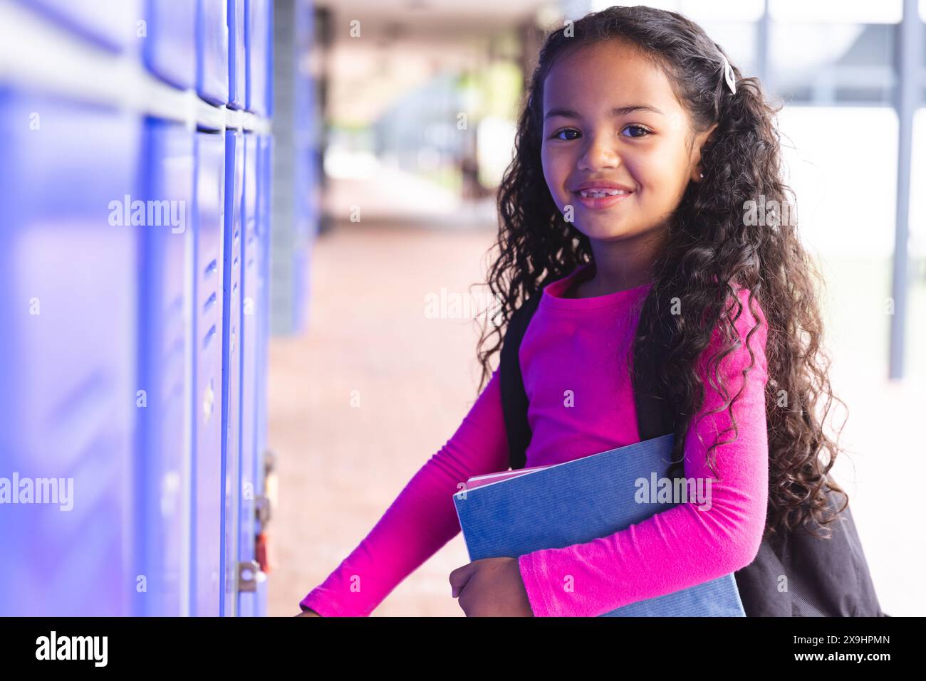 A scuola, giovane studentessa birazziale che tiene libri, in piedi accanto a armadietti all'aperto Foto Stock