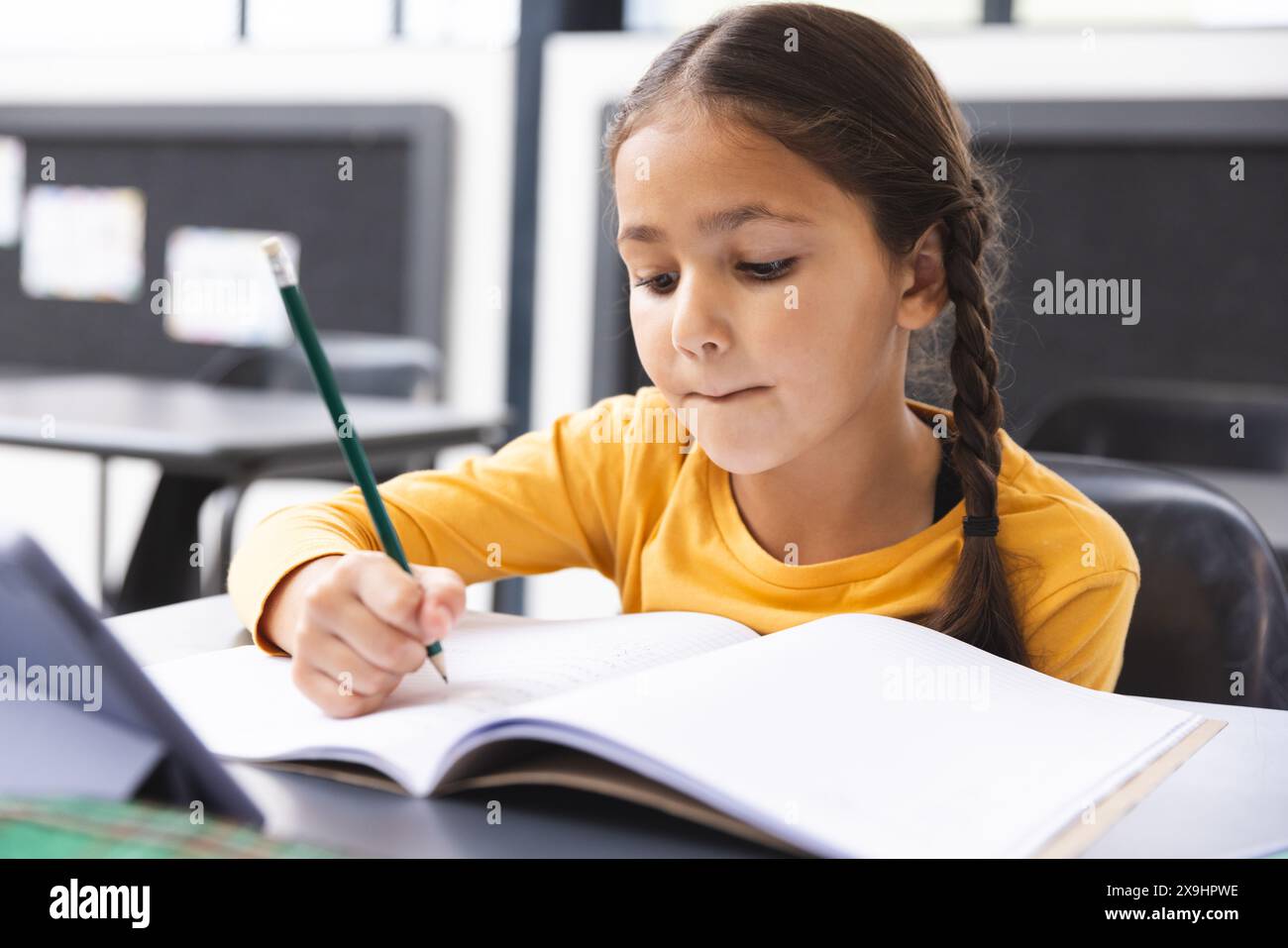 A scuola, giovane ragazza birazziale con capelli intrecciati che si concentra sulla scrittura in classe Foto Stock