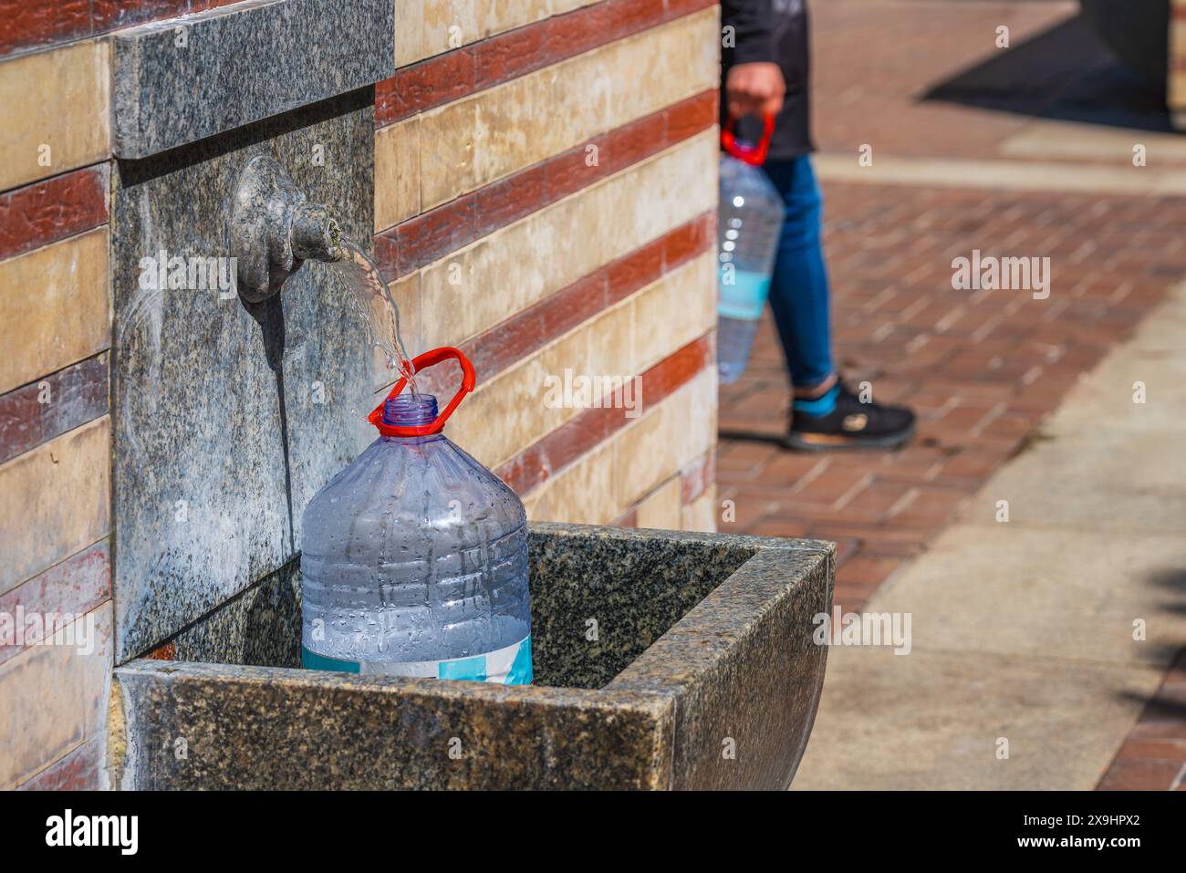 Una grande bottiglia di plastica viene riempita con acqua proveniente da una sorgente termale nel centro di Sofia, Bulgaria Foto Stock