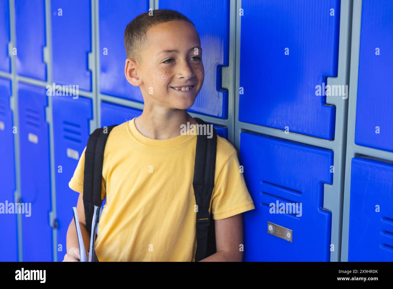 Il ragazzo birazziale sta accanto agli armadietti blu a scuola Foto Stock