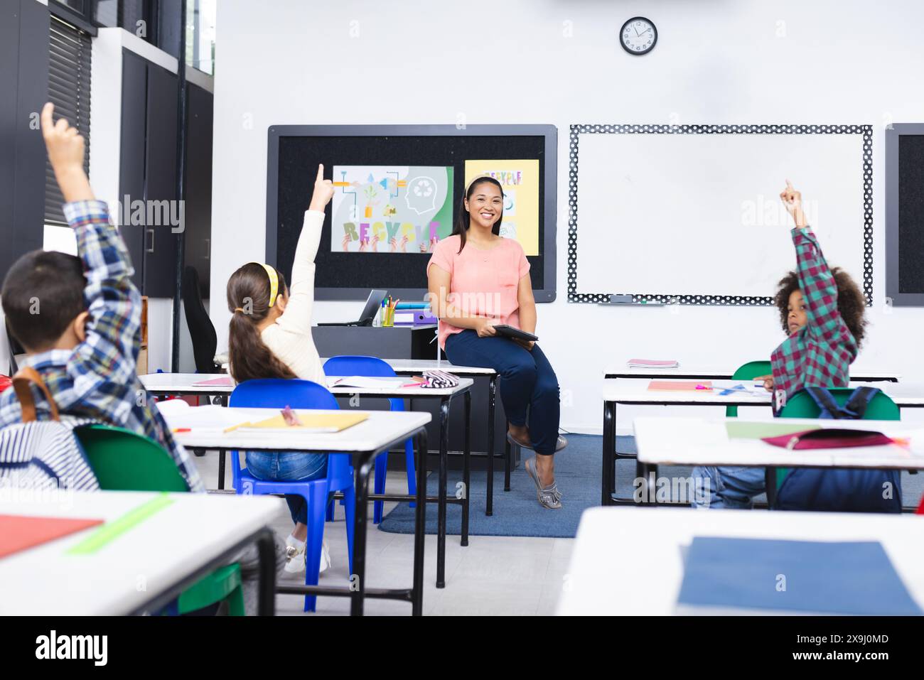 A scuola, la giovane insegnante birazziale sorride agli studenti che alzano le mani in classe Foto Stock