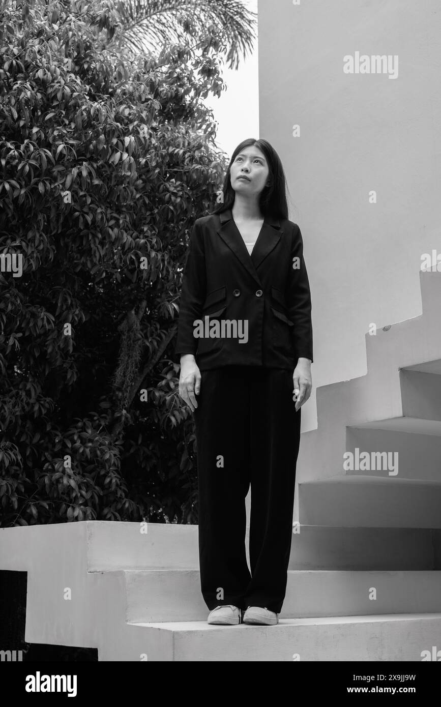 Ritratto monocromatico di una donna professionista in un abbigliamento da lavoro che trasuda fiducia nei moderni passi architettonici Foto Stock