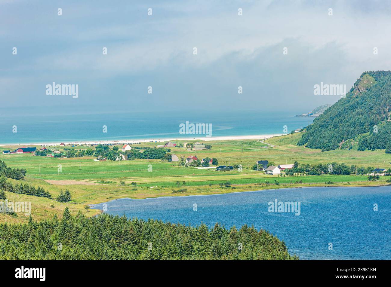 Questa immagine mostra una vista mozzafiato di un piccolo villaggio costiero annidato tra lussureggianti campi verdi e un lago blu scintillante in Norvegia. Il villaggio Foto Stock