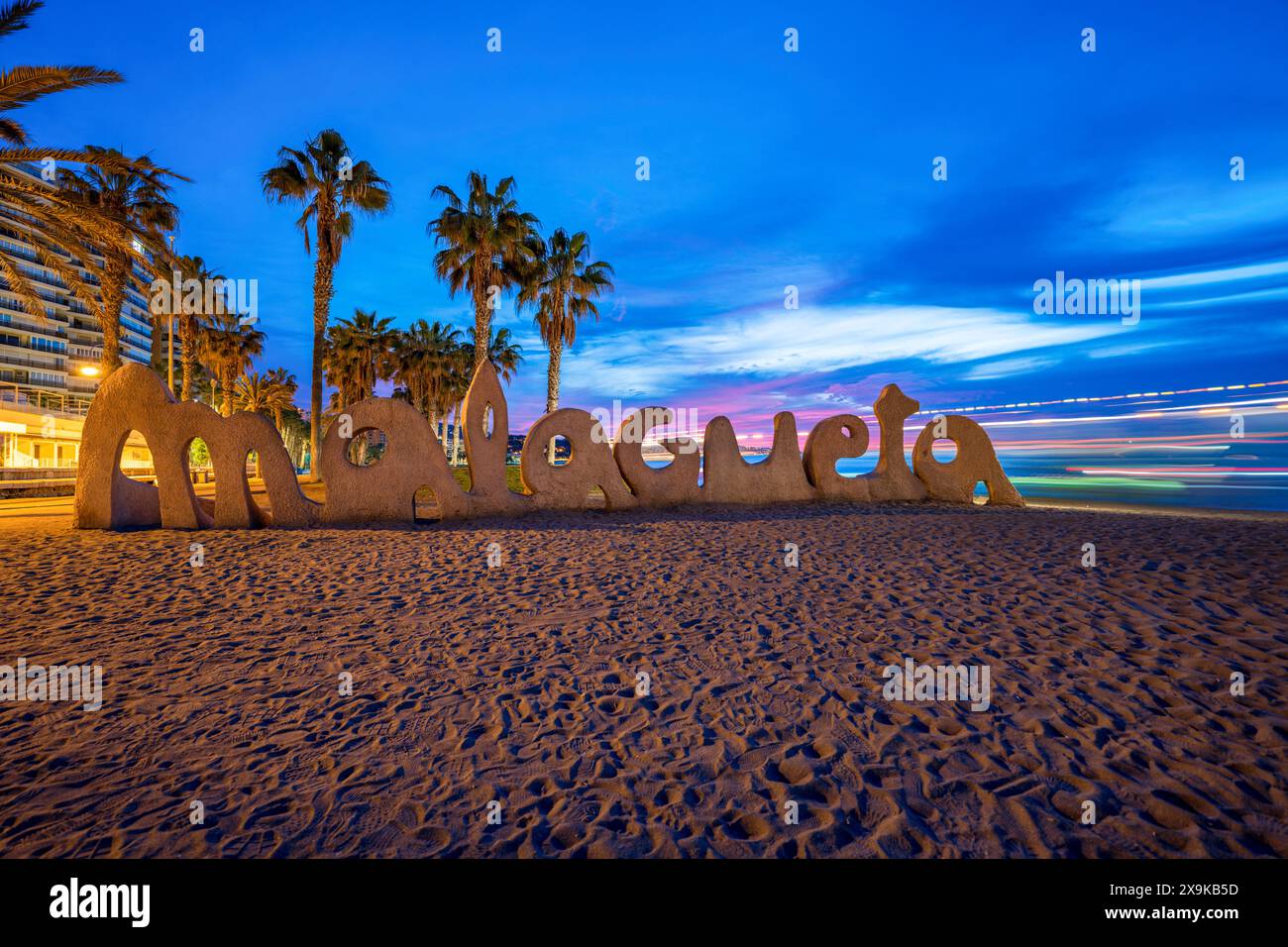 Spiaggia di Malaga, Spagna, con un cartello di Malagueta. Vista panoramica dello skyline della spiaggia di Málaga con cielo blu e sentieri luminosi al tramonto, al tramonto, senza persone. Foto Stock