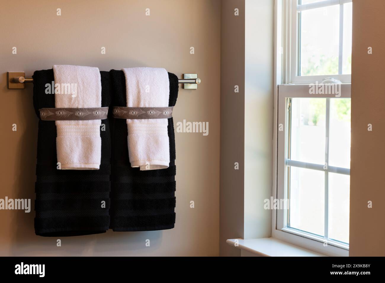 Invitante ambiente da bagno con asciugamani ben ripiegati su una griglia, illuminati dalla luce naturale del sole che scorre attraverso la finestra del bagno. Conc. Immobiliare Foto Stock