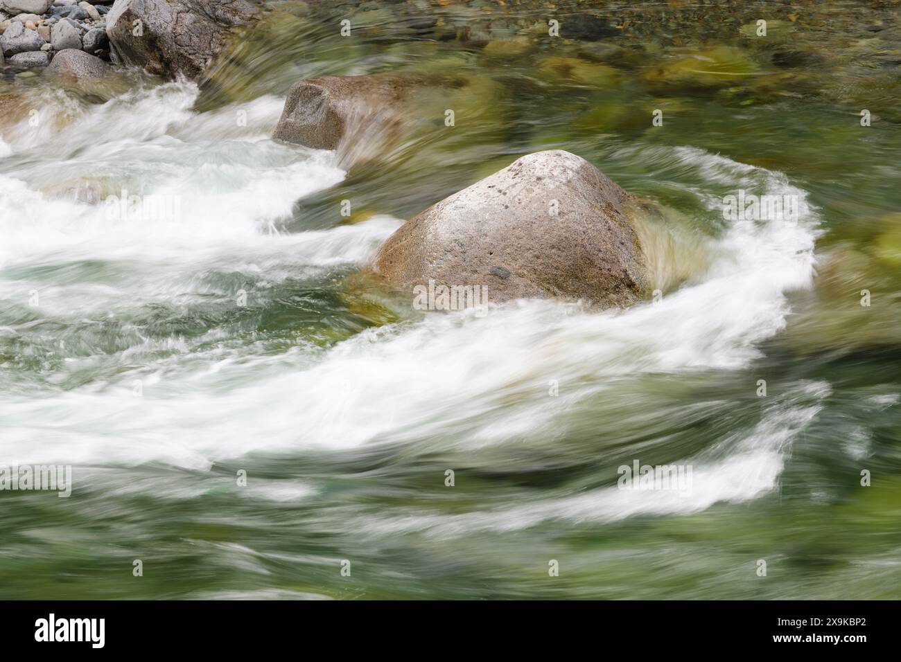 Il flusso d'acqua dolce pulita scorre al rallentatore con linee setose intorno alla roccia del fiume in primavera Foto Stock