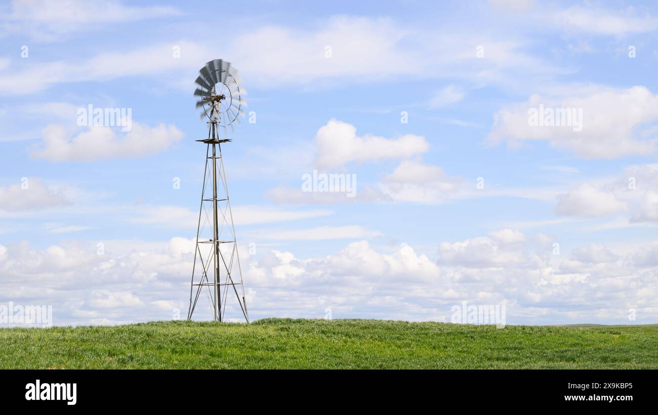 Classico mulino a vento in terreni agricoli verdi con lame sfocate che ruotano sulla torre con nuvole Foto Stock
