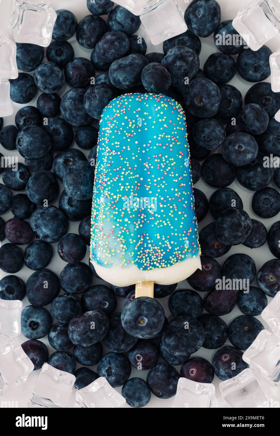 Layout estivo realizzato con gelateria blu smaltata, mirtilli freschi e cubetti di ghiaccio su sfondo bianco. Concept creativo estivo minimalista. Foto Stock