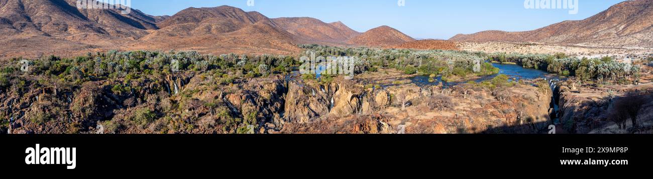Panorama, fiume Kunene con vegetazione verde nel paesaggio secco delle montagne rosse, cascata e baobab africano (Adansonia digitata), alla luce della sera Foto Stock