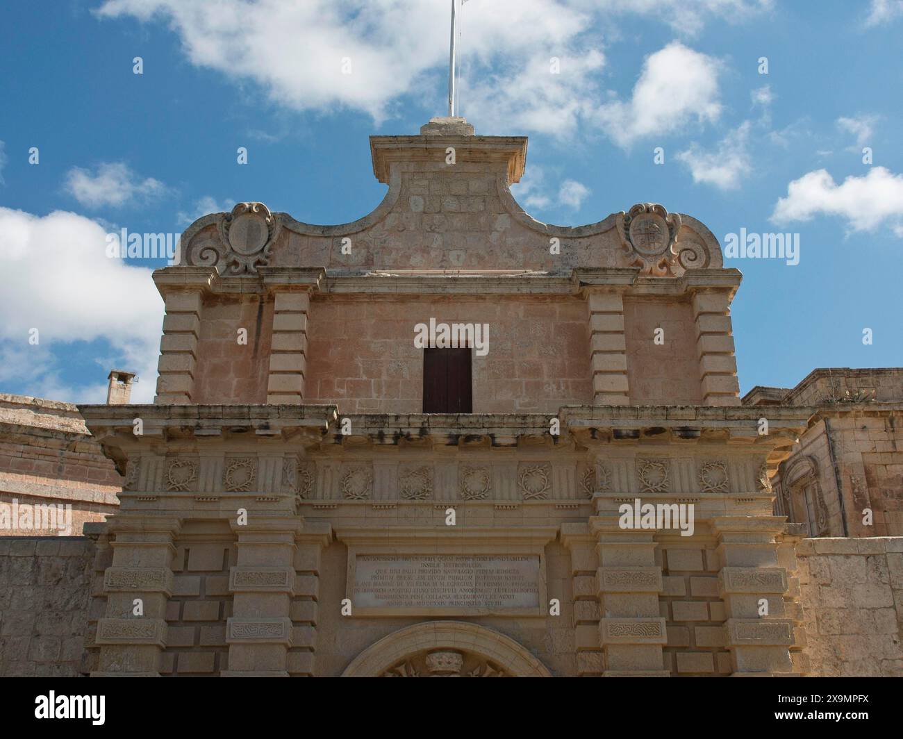 Ingresso di un edificio storico con arcata in pietra decorata sotto il cielo blu con nuvole, la città di mdina sull'isola di malta con la sua storia Foto Stock