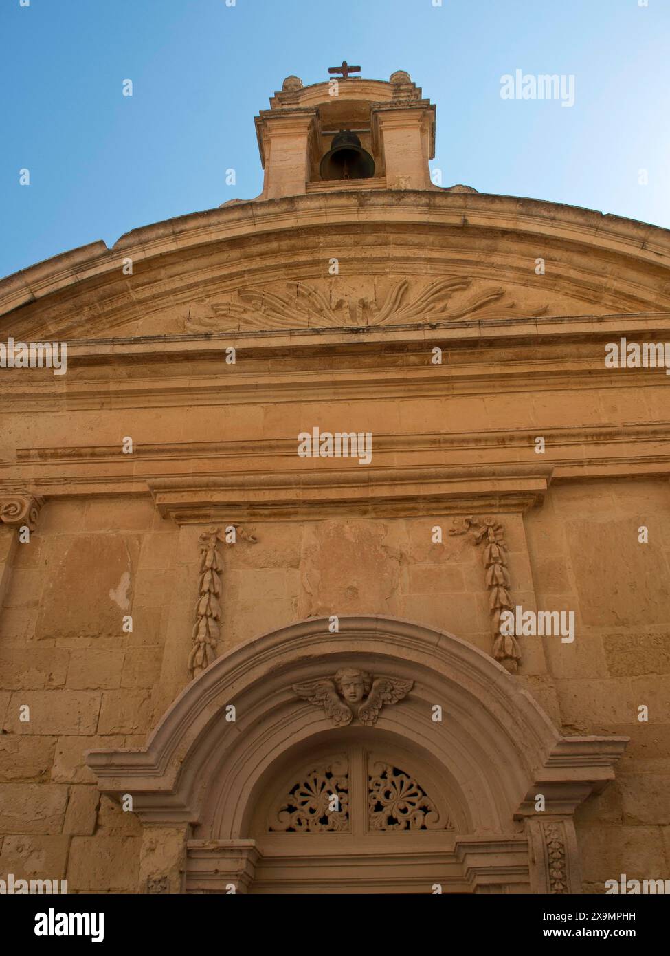 Facciata di una chiesa storica con un campanile ornato sotto un cielo azzurro, la città di mdina sull'isola di malta con case storiche Foto Stock