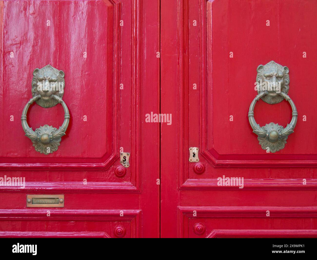 Due luccicanti porte rosse con antichi battitori decorativi a testa di leone, la città di mdina, sull'isola di malta, con case storiche colorate Foto Stock