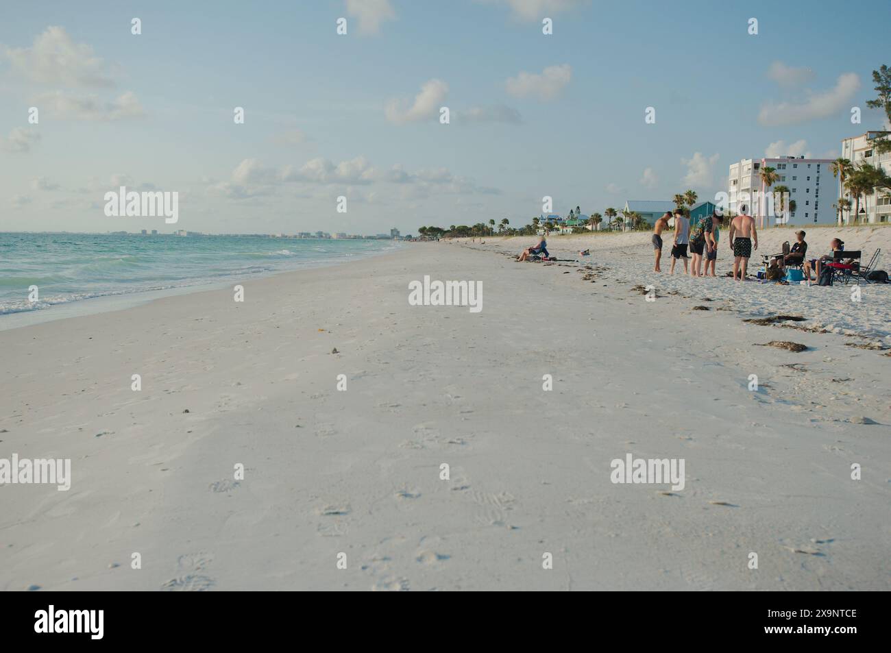 Ampia vista della spiaggia Pass-a-Grille di St. Pete Beach, Florida, guardando a nord. Rocce e molte persone camminano nella sabbia e nell'acqua, vicino al tramonto Foto Stock