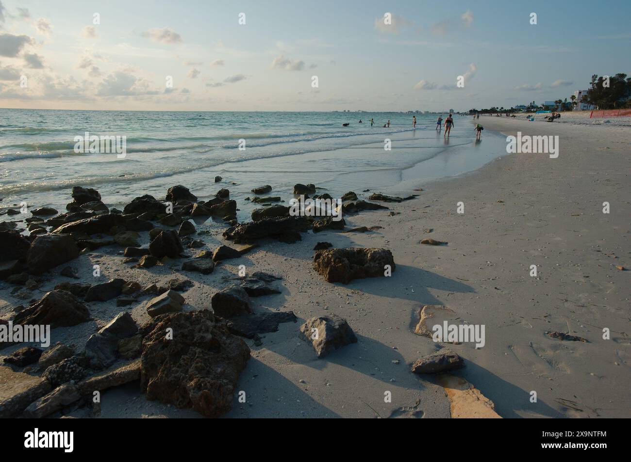 Ampia vista della spiaggia Pass-a-Grille di St. Pete Beach, Florida, guardando a nord. Rocce e molte persone camminano nella sabbia e nell'acqua, vicino al set Foto Stock