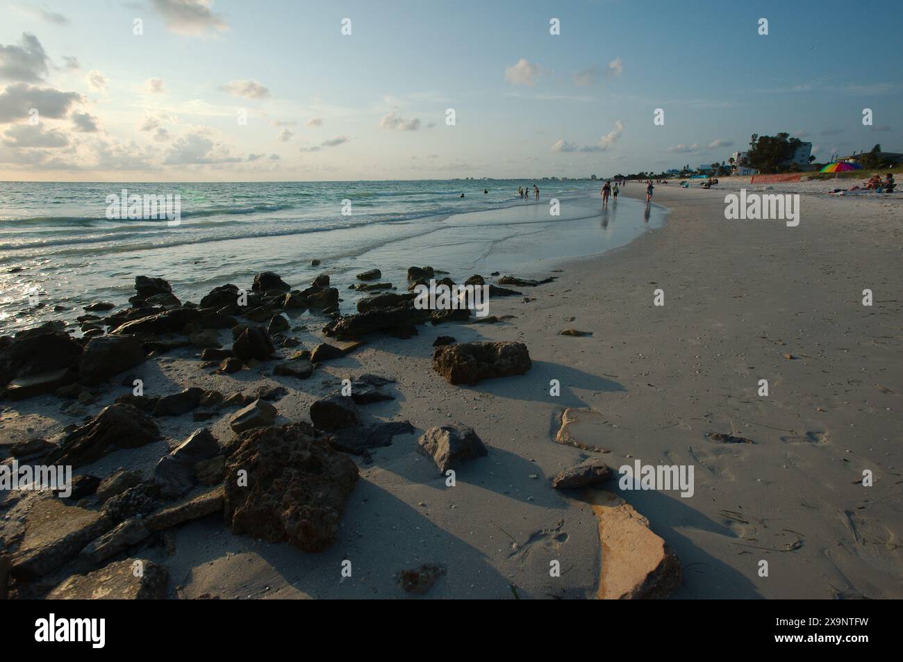 Ampia vista della spiaggia Pass-a-Grille di St. Pete Beach, Florida, guardando a nord. Rocce e molte persone camminano nella sabbia e nell'acqua, vicino al set Foto Stock