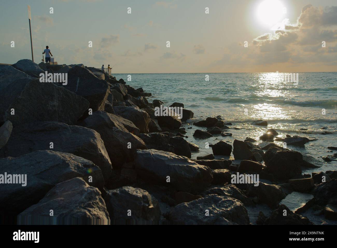 Tramonto con silhouette scura alla spiaggia Pass-a-Grille di St Petersburg, Florida, vista su grandi rocce rocciose al molo. Scarsa illuminazione con gente che pesca. D'oro Foto Stock
