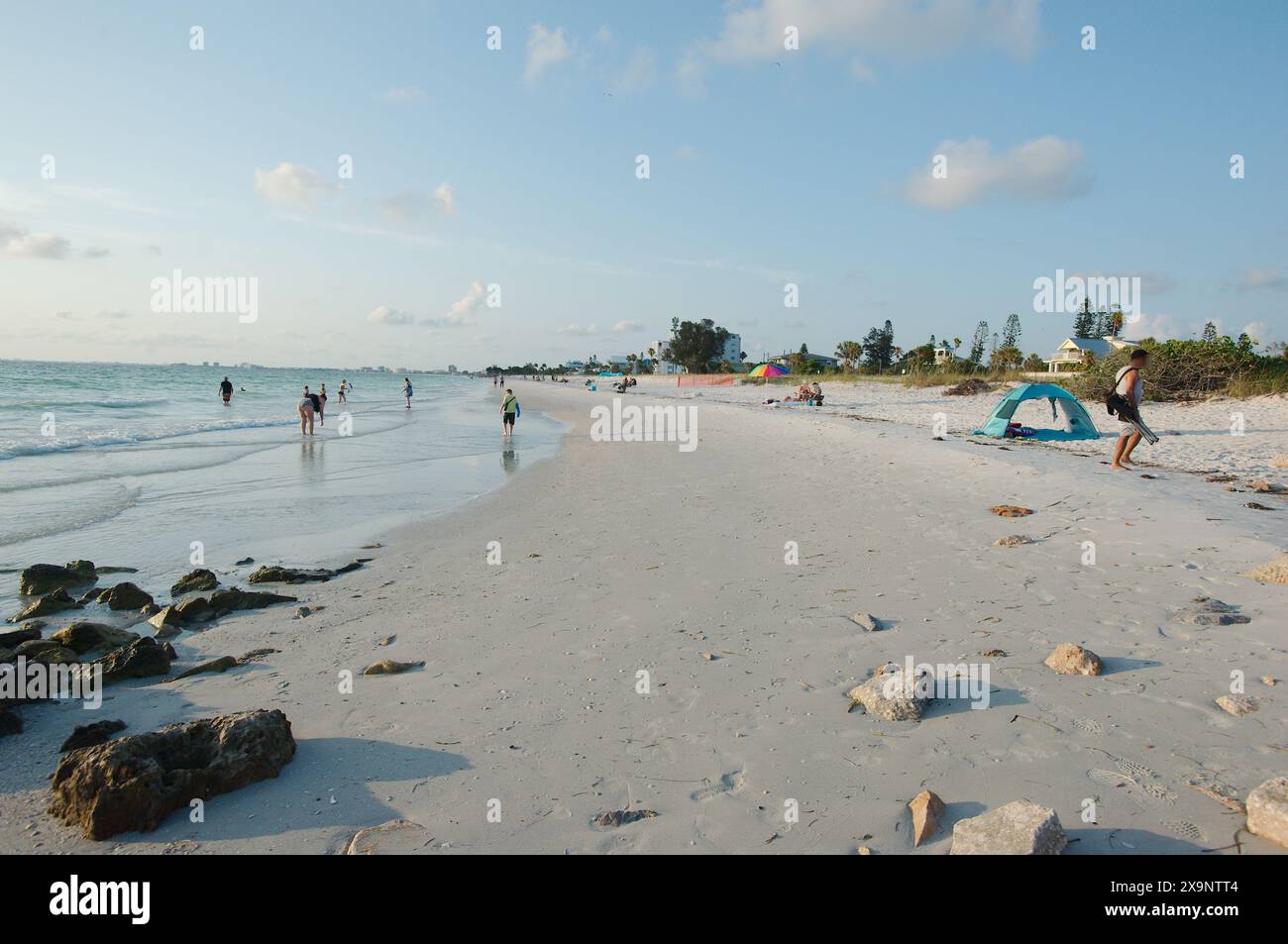 Ampia vista della spiaggia Pass-a-Grille di St. Pete Beach, Florida, guardando a nord. Rocce e molte persone camminano nella sabbia e nell'acqua, vicino al set Foto Stock