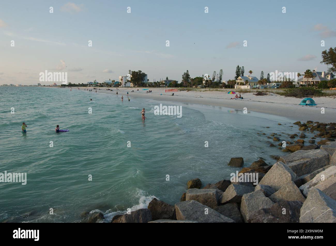 Ampia vista della spiaggia Pass-a-Grille di St. Pete Beach, Florida, guardando a nord. Rocce e molte persone camminano nella sabbia e nell'acqua, vicino al set Foto Stock