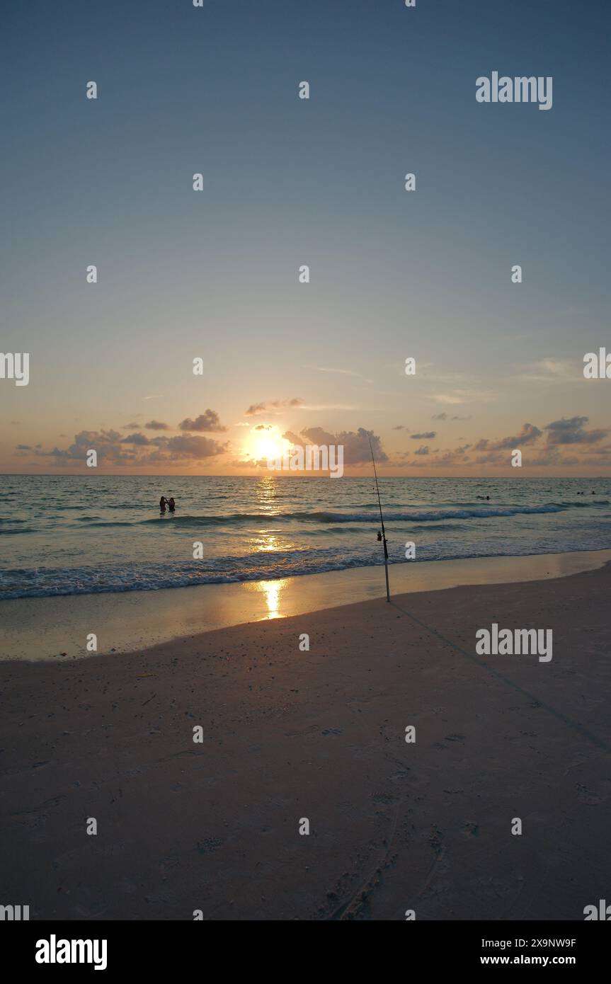 Tramonto alla spiaggia Pass-a-Grille di St Petersburg, Florida. Scarsa illuminazione con più persone in acqua. Bagliore d'oro e cielo blu del sole nella parte posteriore. Foto Stock