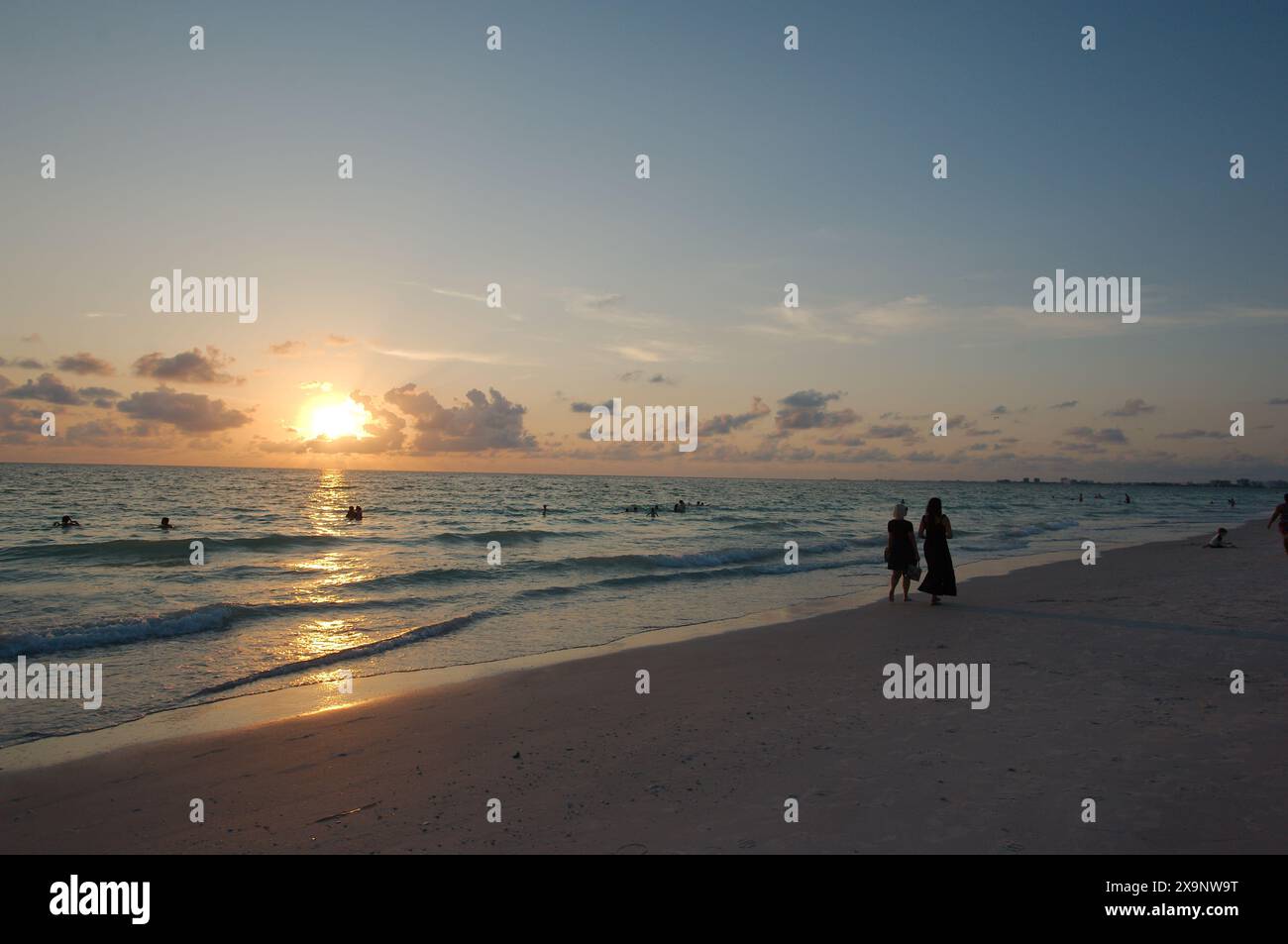 Tramonto alla spiaggia Pass-a-Grille di St Petersburg, Florida. Scarsa illuminazione con più persone in acqua. Bagliore dorato e cielo blu del Sole orizzontale Foto Stock