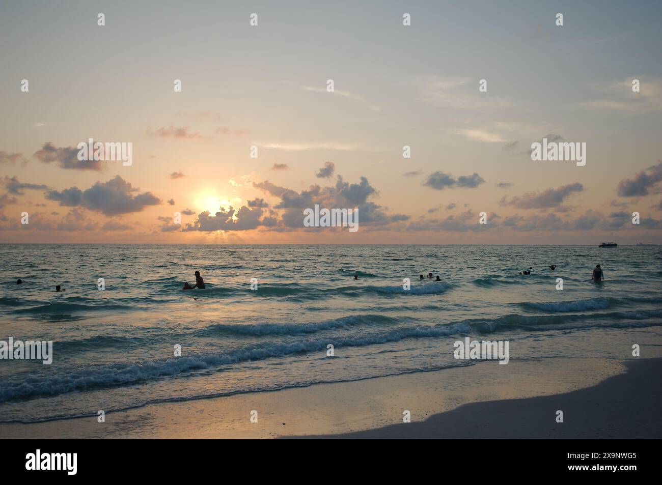 Tramonto alla spiaggia Pass-a-Grille di St Petersburg, Florida. Scarsa illuminazione con più persone in acqua. Bagliore dorato e cielo blu del Sole orizzontale Foto Stock