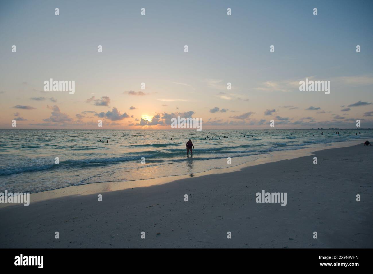 Tramonto alla spiaggia Pass-a-Grille di St Petersburg, Florida. Scarsa illuminazione con più persone in acqua. Bagliore dorato e cielo blu del Sole orizzontale Foto Stock