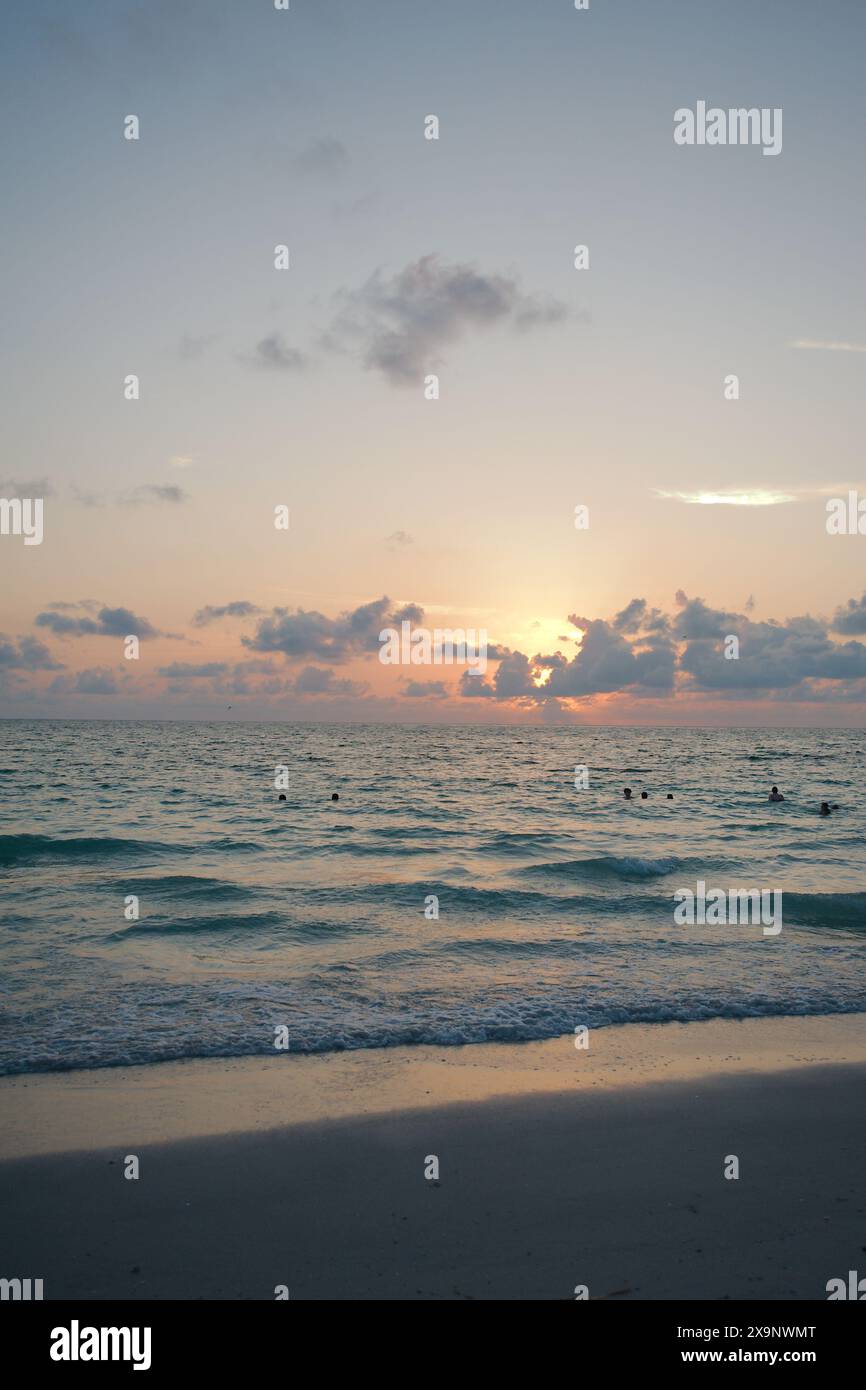 Tramonto alla spiaggia Pass-a-Grille di St Petersburg, Florida. Scarsa illuminazione con più persone in acqua. Bagliore d'oro e cielo blu del sole nella parte posteriore. Foto Stock