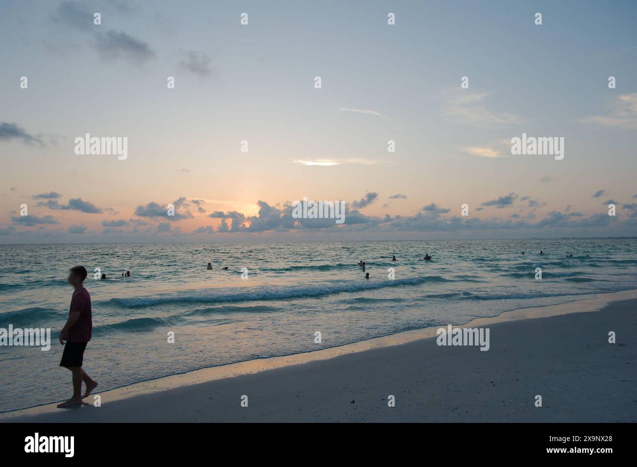 Tramonto alla spiaggia Pass-a-Grille di St Petersburg, Florida. Scarsa illuminazione con più persone in acqua. Bagliore dorato e cielo blu del Sole orizzontale Foto Stock