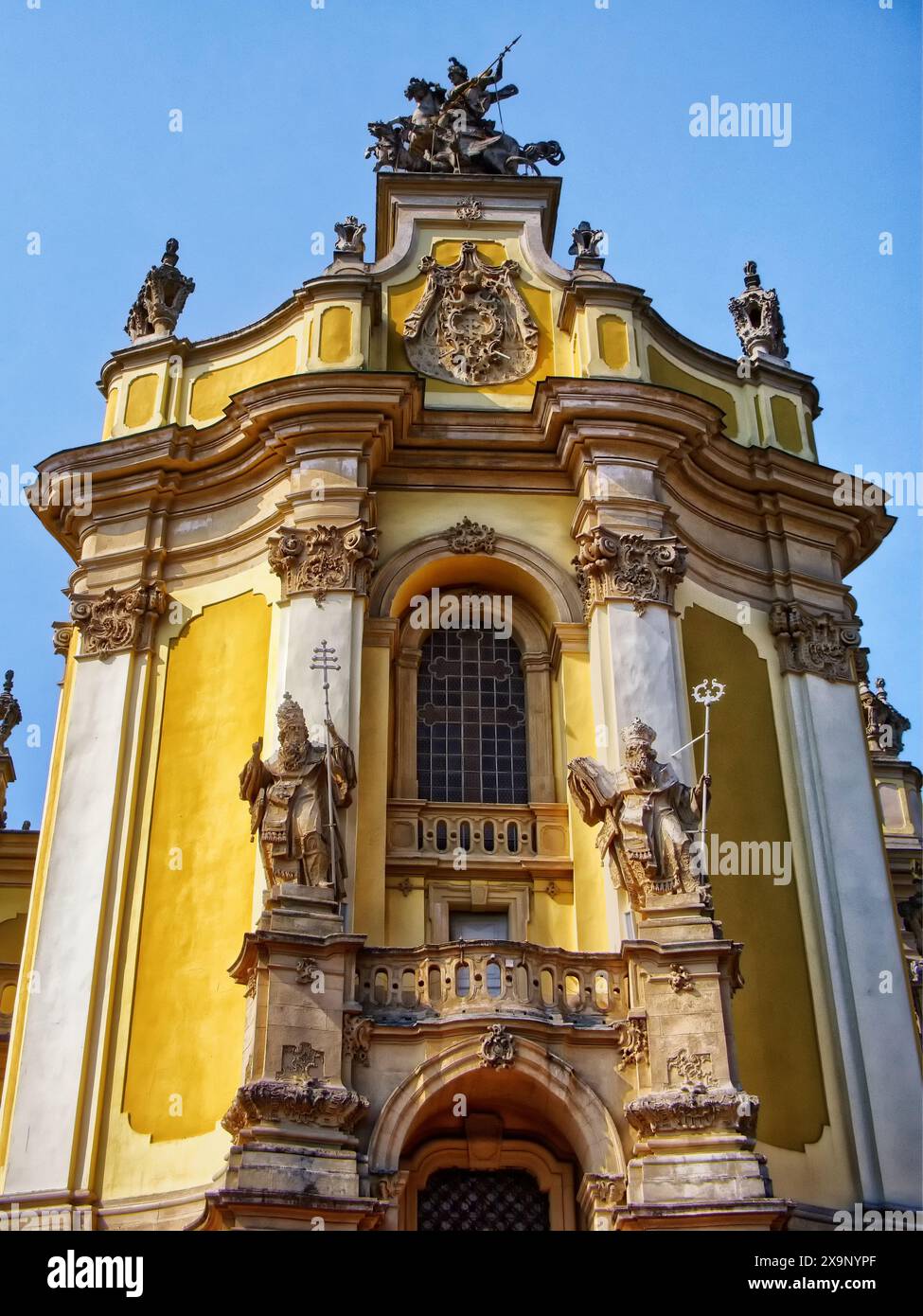 Facciata della chiesa barocca: Una facciata barocca con sculture ornate sotto un cielo blu limpido, che riflette l'architettura storica. St. George's Cathedr Foto Stock