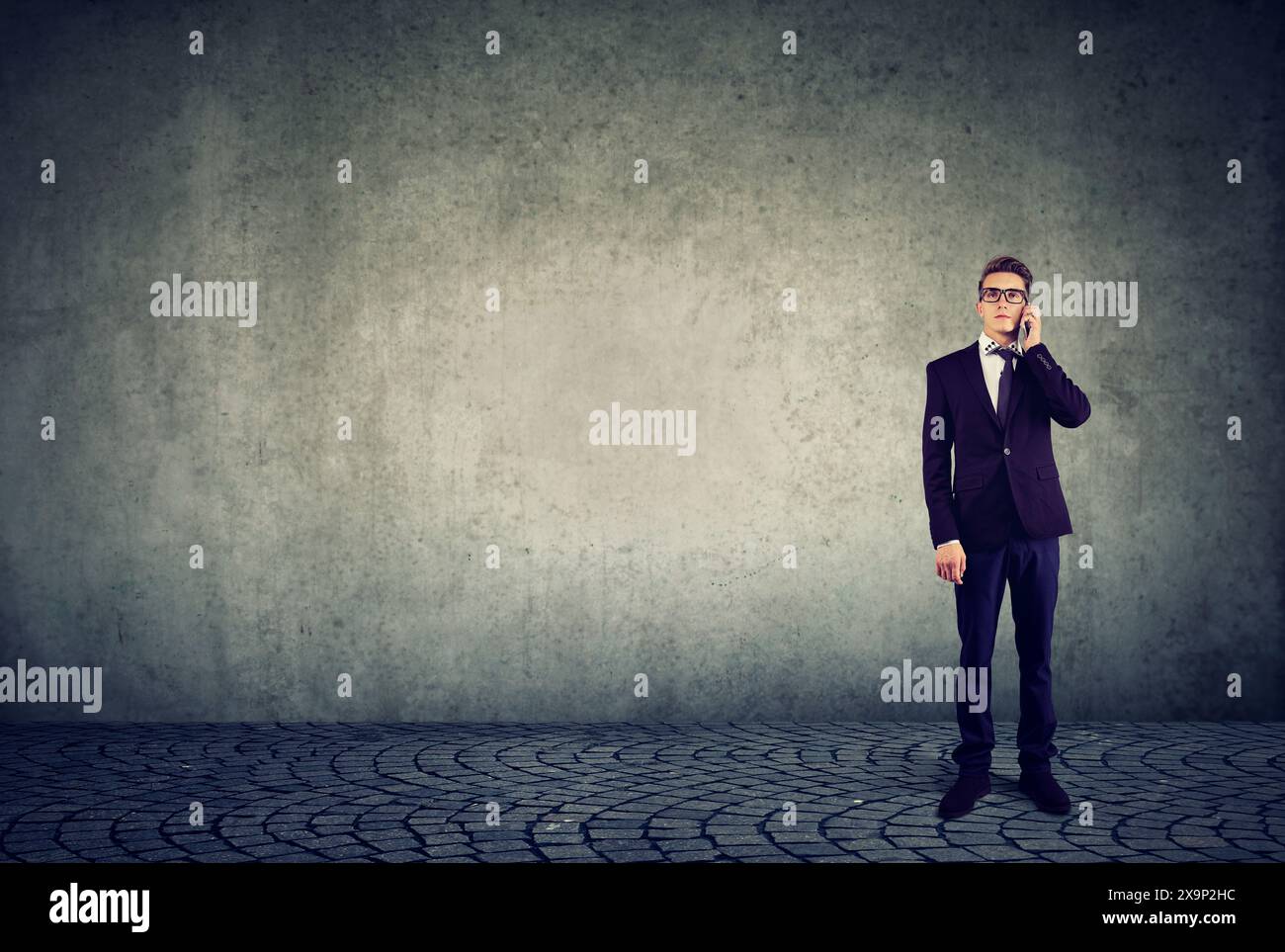 Uomo d'affari in piedi al muro e a parlare al cellulare Foto Stock