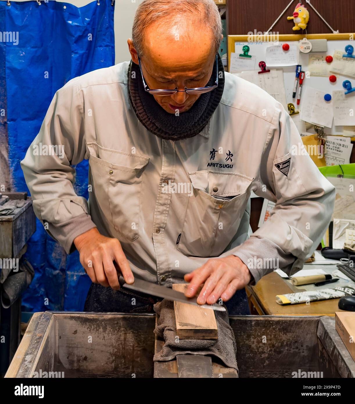 Un abile artigiano affila con cura una lama su una pietra per affilare, concentrandosi sul suo mestiere Foto Stock