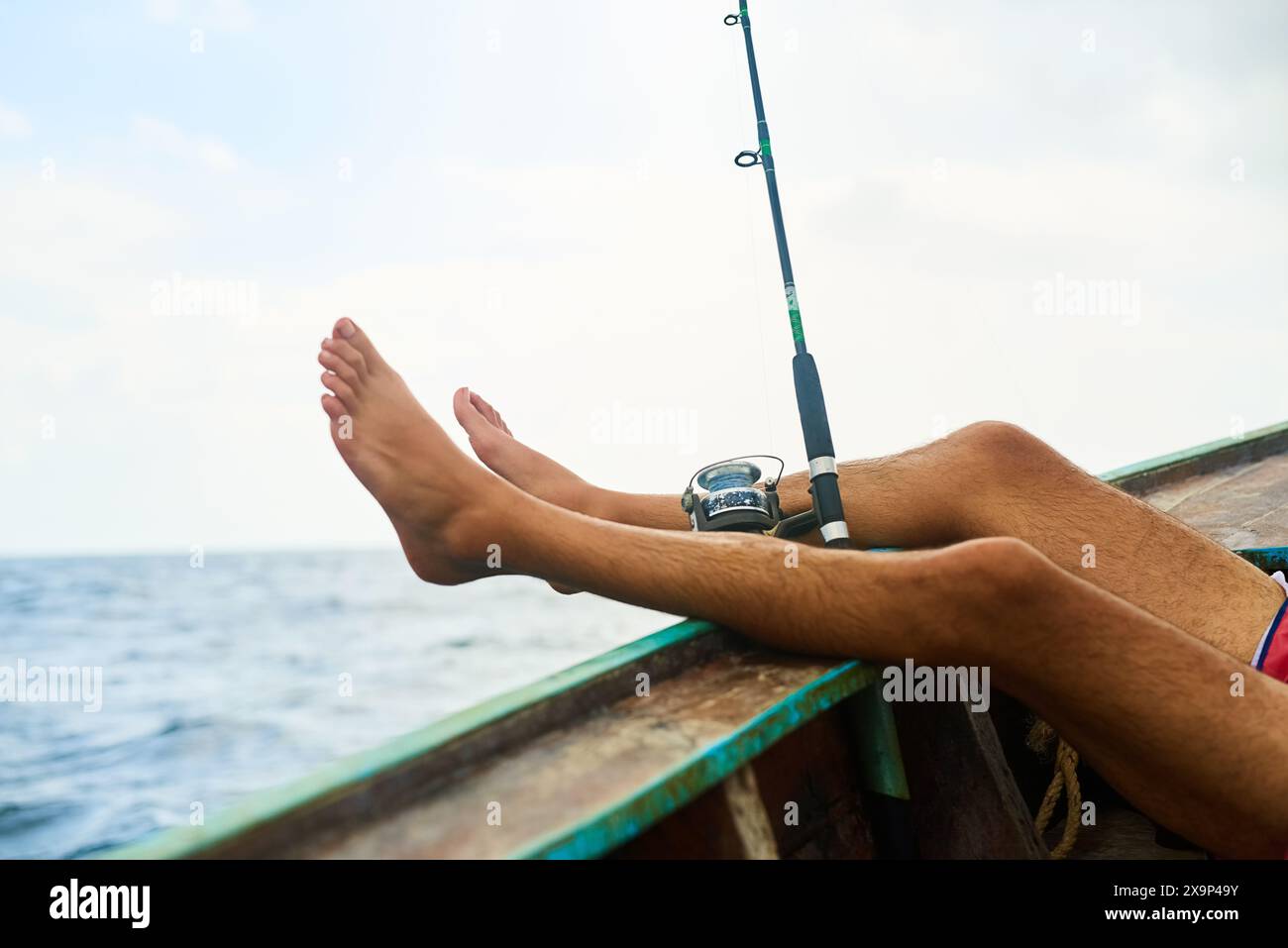 Uomo, piedi e barca per pescare nell'oceano con relax, vacanza con attività acquatiche per il benessere. Uomo, gambe in alto e mare con pausa di lancio sulla nave Foto Stock