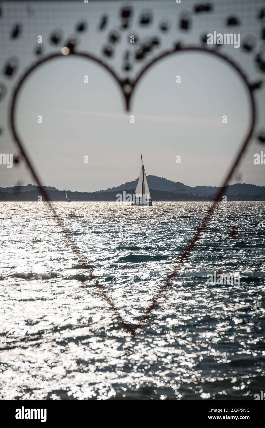 Barca a vela in mare durante il tramonto, vista attraverso la decorazione a forma di cuore Foto Stock