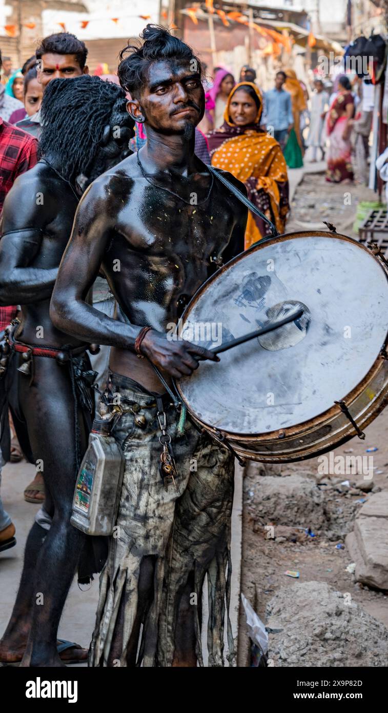 L'uomo coperto di cenere suona un grande tamburo durante una celebrazione culturale con gli spettatori sullo sfondo Foto Stock