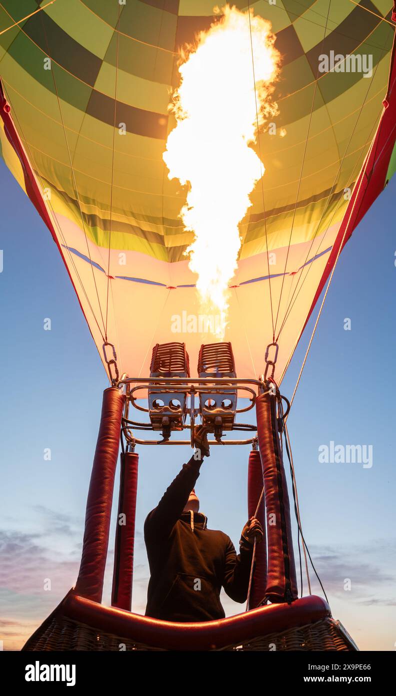 Un pilota aziona il bruciatore di una vibrante mongolfiera, generando un potente getto di fiamma, mentre il cielo dell'alba si schiarisce sullo sfondo. fiamma pilota Foto Stock