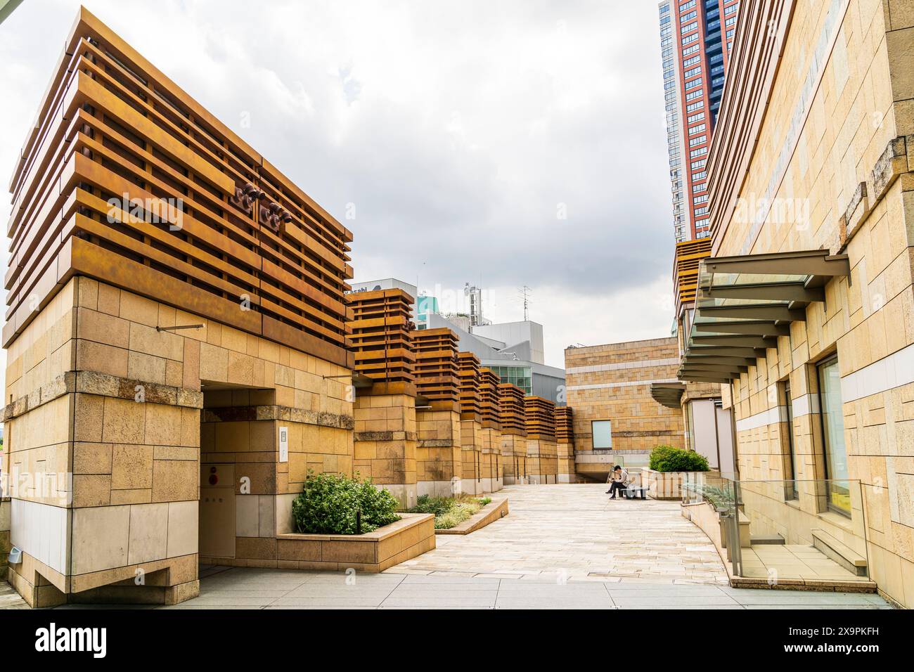 Passerella tra la Torre Mori e una serie di strutture quadrate con un uomo solitario seduto su una panchina nell'area Hillside di Roppongi Hills, Tokyo. Foto Stock