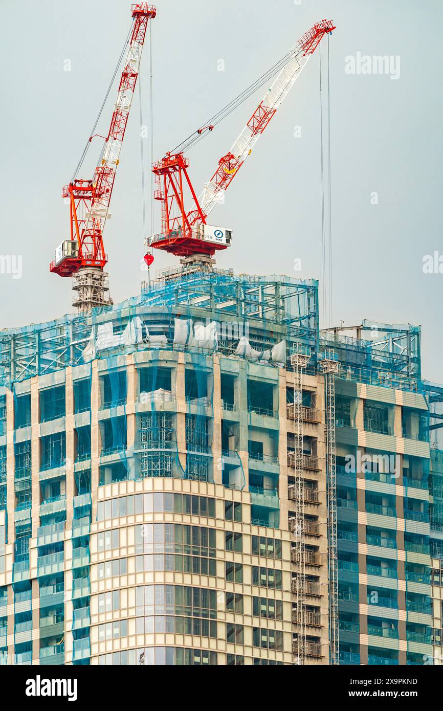 Teleobiettivo di due gru rosse e bianche in cima a un alto edificio di uffici in costruzione a Roppongi a Tokyo. Sfondo nuvola grigia sovradimensionato. Foto Stock