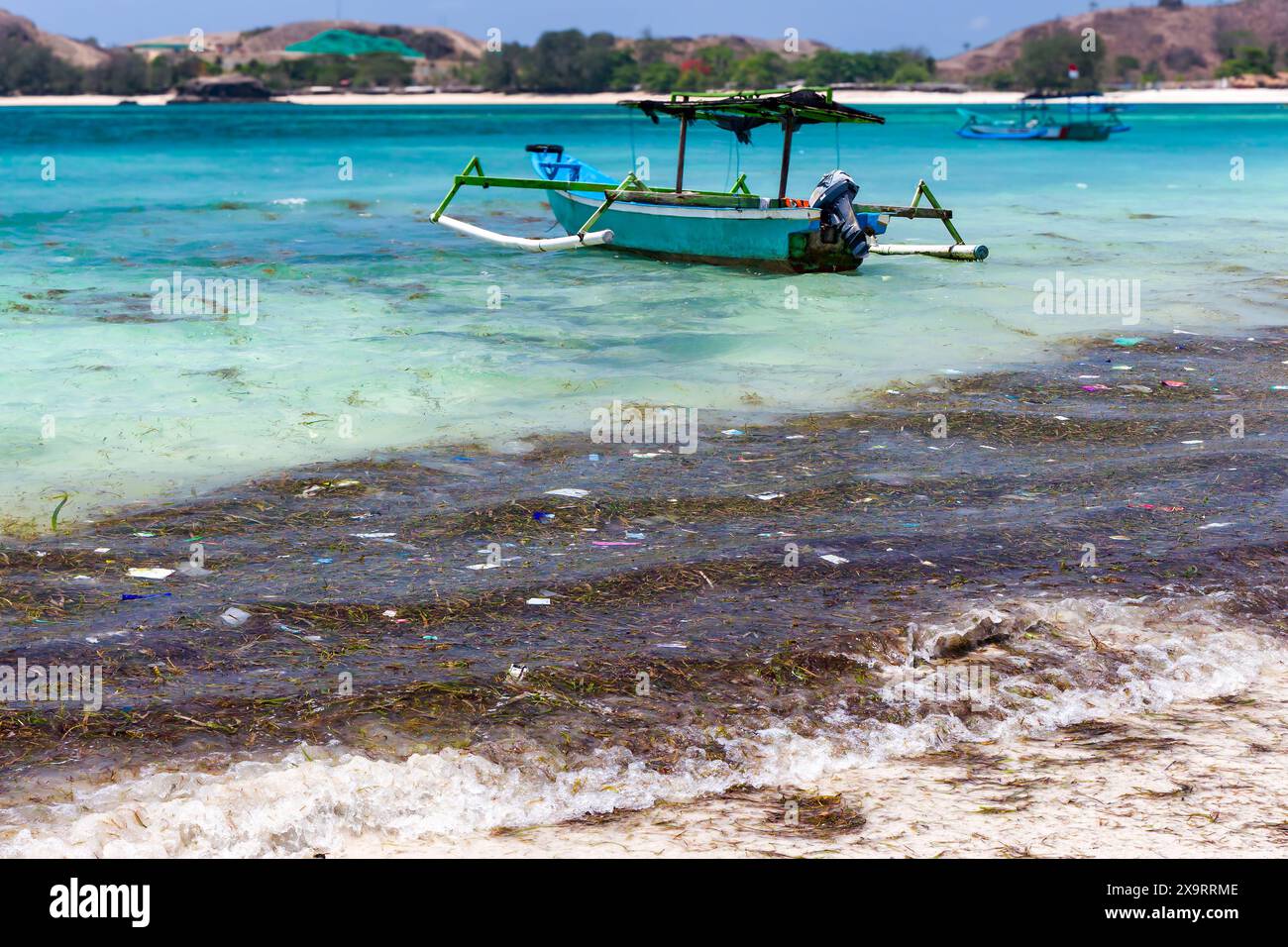 Barca accanto alla plastica galleggiante e alla spazzatura in un caldo oceano tropicale a Tanjung Aan, Lombok, Indonesia Foto Stock