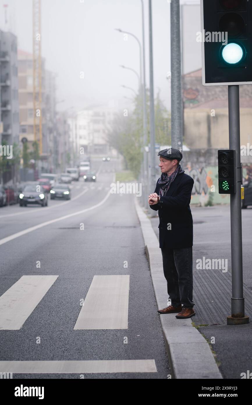 Un elegante uomo di mezza età in piedi di fronte a un passaggio pedonale, che controlla l'ora sul suo orologio da polso. Foto Stock