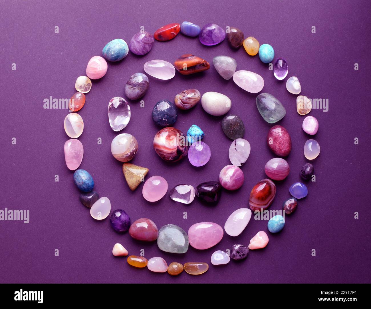 Pietre naturali di diversi colori sono disposte a spirale su sfondo viola. Previsioni, stregoneria, pratica esoterica spirituale. Foto Stock