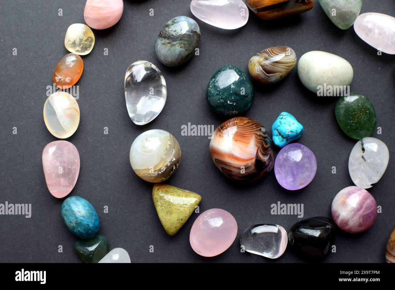 Le pietre naturali di diversi colori sono disposte sotto forma di spirale. Previsioni, stregoneria, pratica esoterica spirituale. Foto Stock
