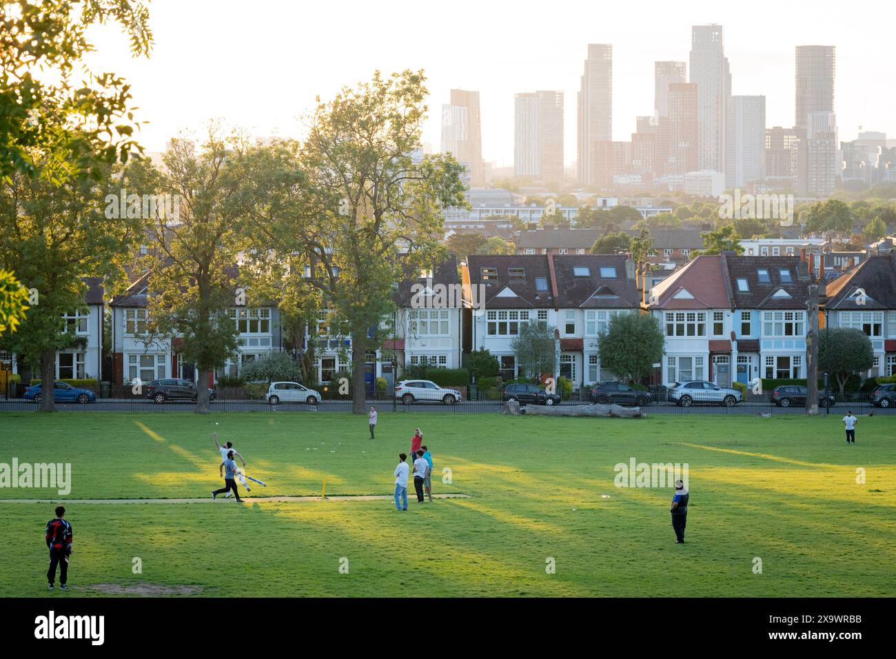 I giocatori dilettanti di cricket godono della luce del sole della domenica sera sullo sfondo di uno skyline a sud di Londra di grattacieli a Nine Elms a Battersea, visto da Ruskin Park, uno spazio verde pubblico a Lambeth, il 2 giugno 2024, a Londra, Inghilterra. Foto Stock