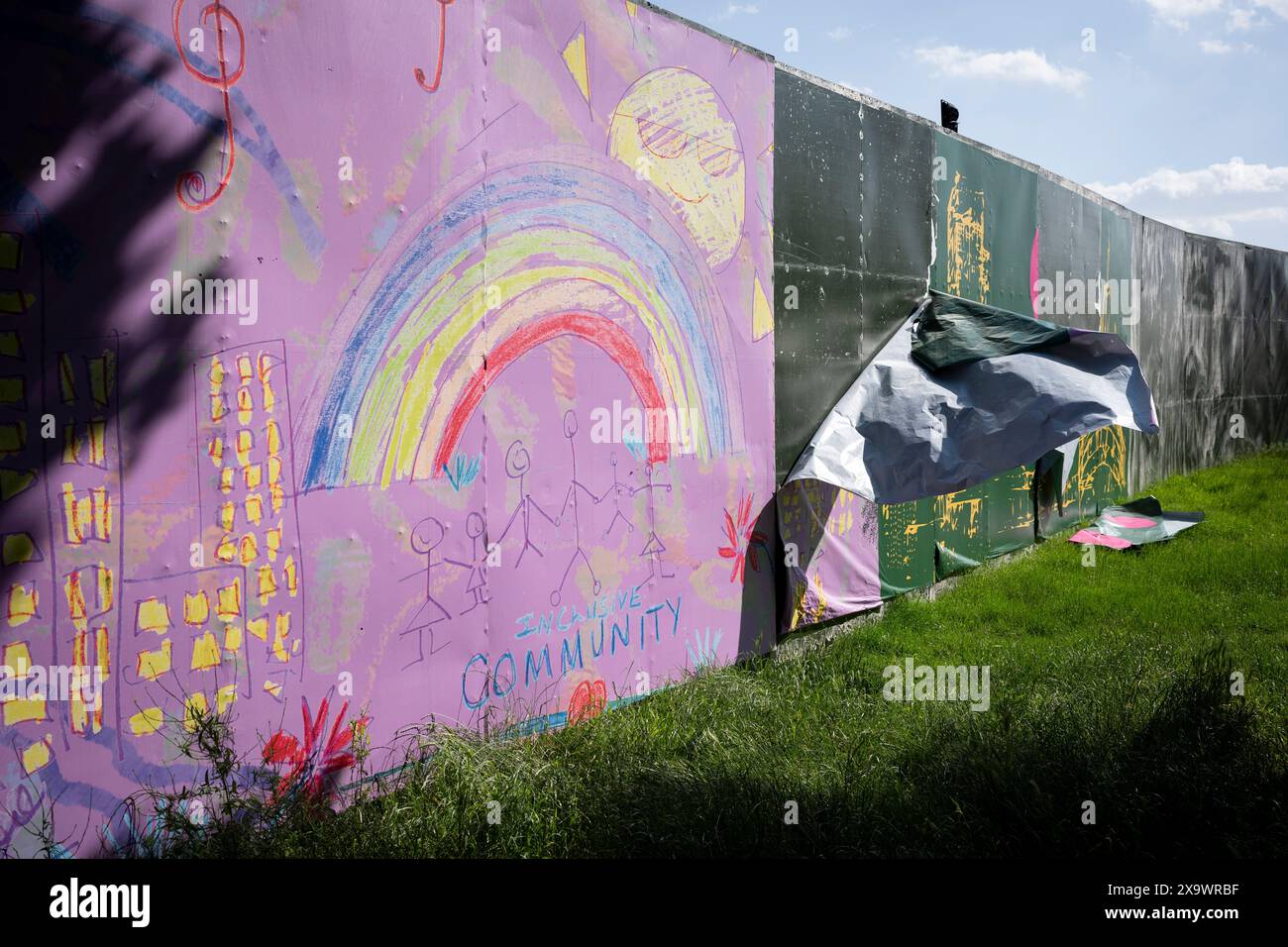 Un paesaggio di uno schermo perimetrale che circonda Brockwell Park durante il Mighty Hoopla festival per la comunità LGBTQ+, il 2 giugno 2024, a Londra, Inghilterra. Il disegno di un bambino presenta un arcobaleno, bambini giocanti e un messaggio ironico sulla "Comunità inclusiva" che mette in evidenza l'uso dello spazio verde per le imprese private da parte del Lambeth Council, contro i consigli di quartiere che consegnano parchi pubblici altrimenti goduti dalle comunità locali per molte settimane prima e dopo l'evento stesso. Foto Stock