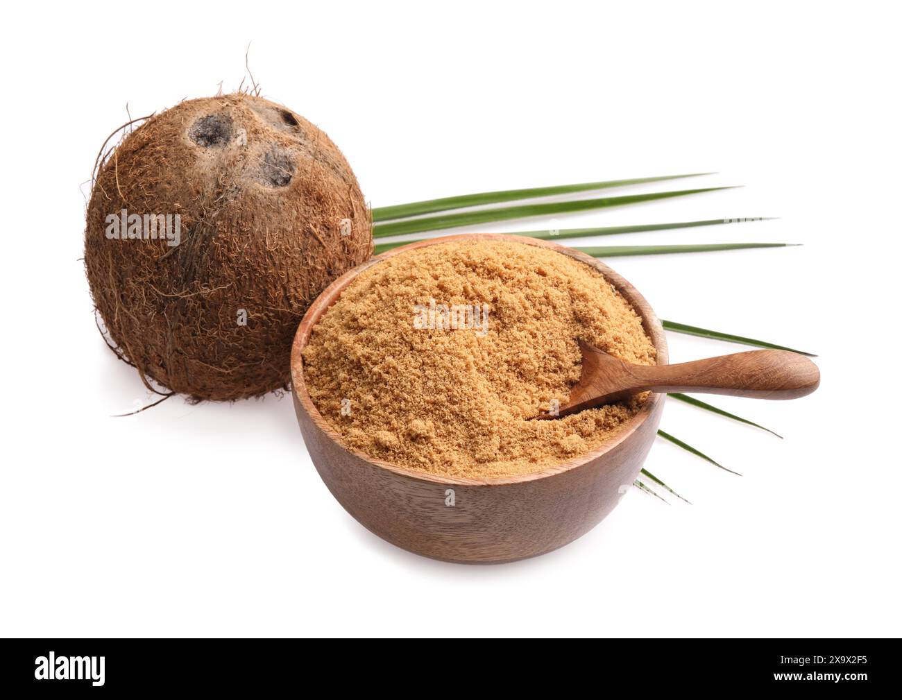 Zucchero di cocco nel recipiente, cucchiaio, frutta e foglie di palma isolate su bianco Foto Stock