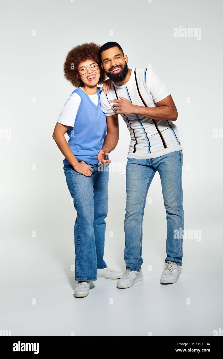 Un uomo e una donna afroamericani in un abbigliamento alla moda che si mettono in posa insieme su uno sfondo grigio. Foto Stock