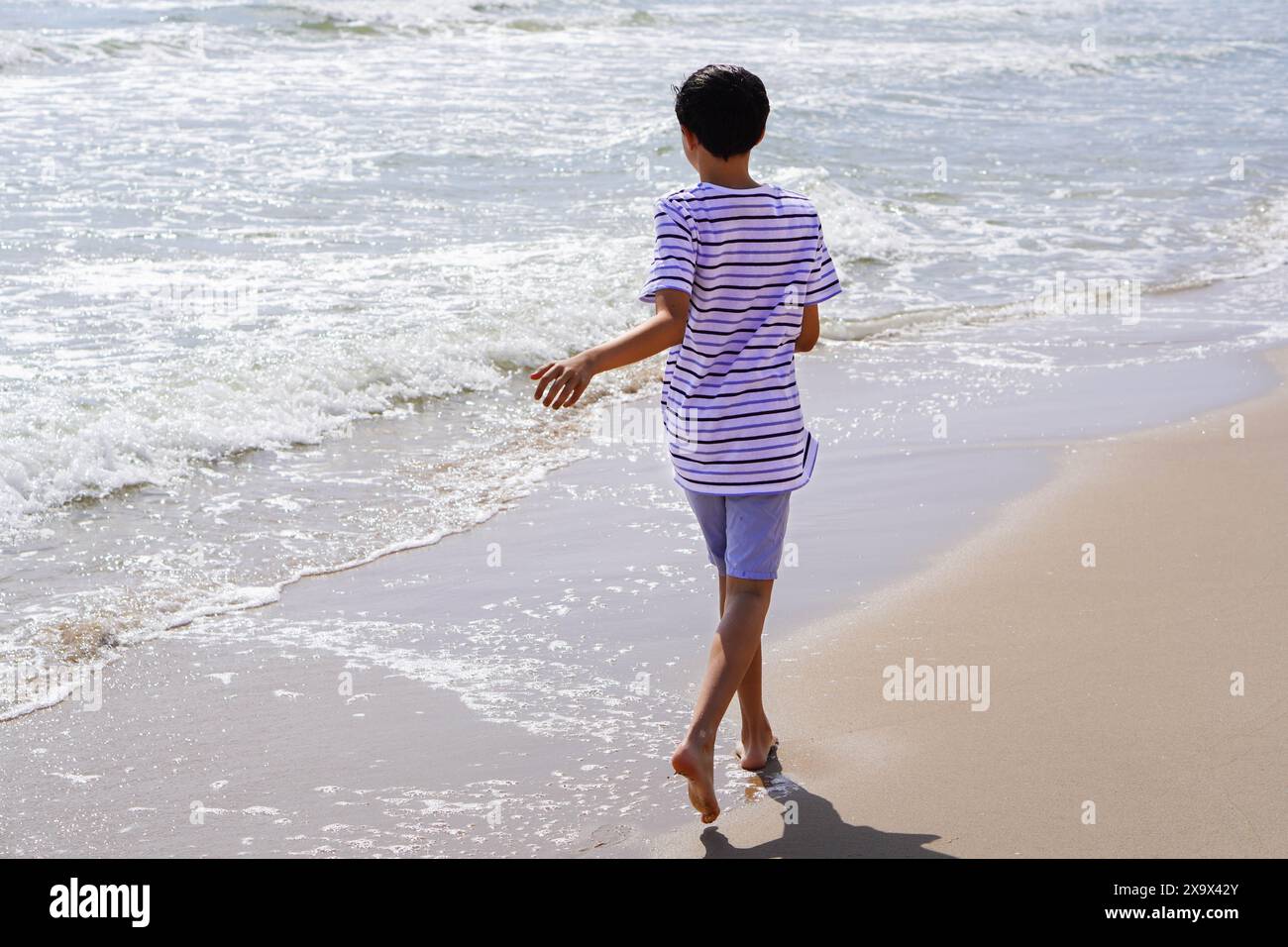 ragazzo sulla schiena che cammina a piedi nudi sulla spiaggia Foto Stock